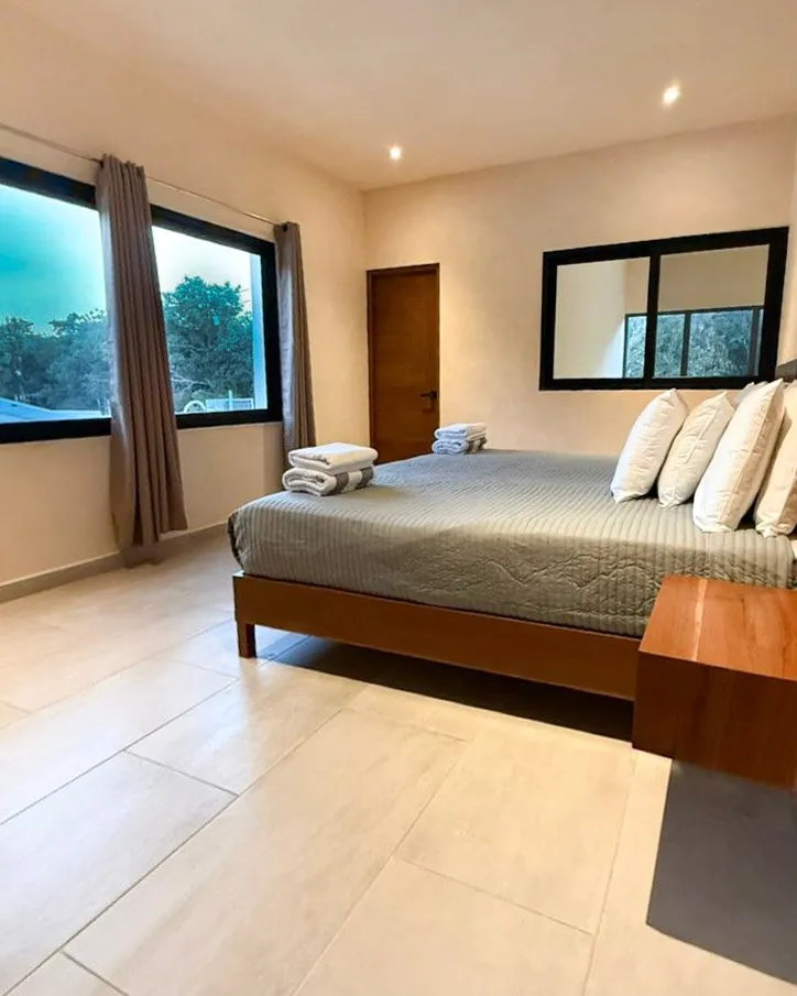 Recámara con cama y ventanales hacia los árboles